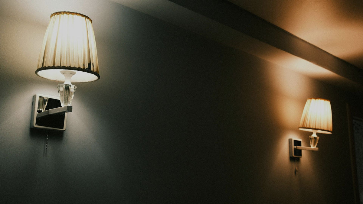Two illuminated wall sconces with pleated shades on dark walls