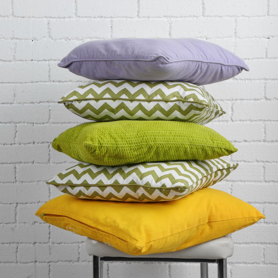 Lavender, green, yellow and chevron throw pillows stacked on stool.