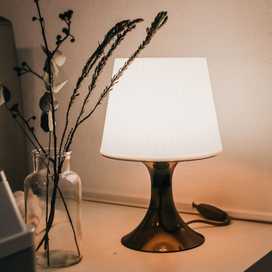  Black table lamp with white shade beside glass branch vase.