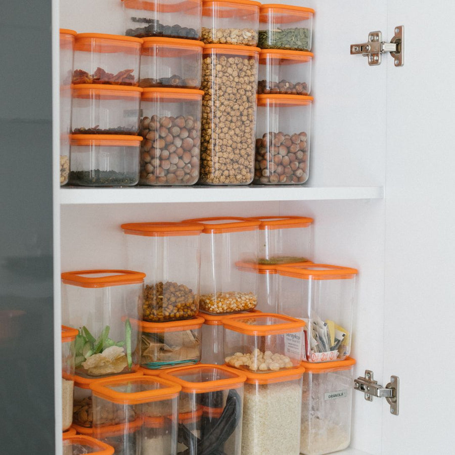 Clear containers with orange lids organizing food inside white cabinet